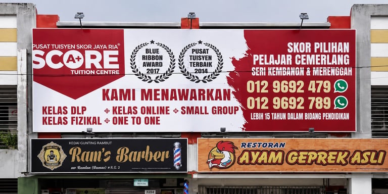 Large red and white storefront sign advertising tutoring center with awards, featuring barber shop and restaurant signage below